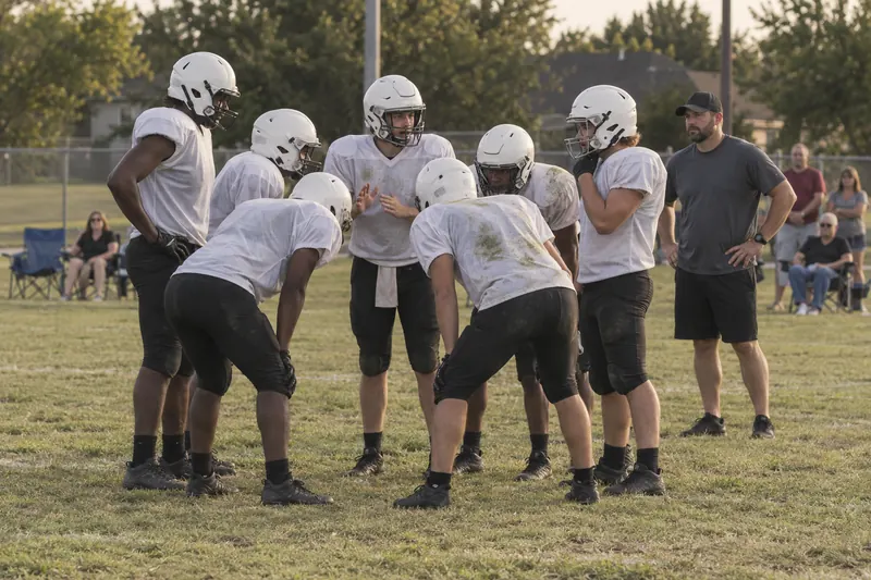 Youth football players in a huddle while their coach looks on